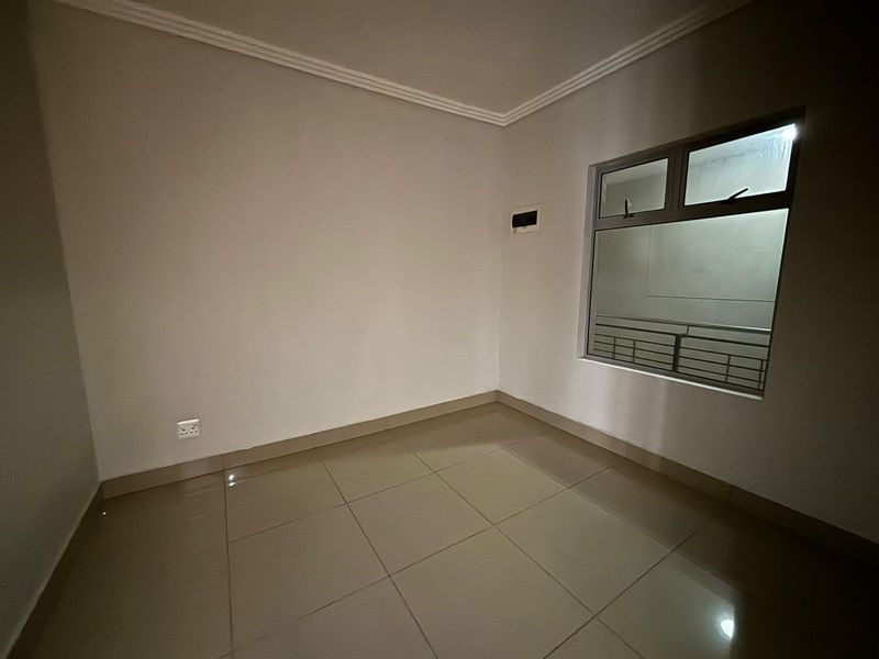 A clean, empty bedroom featuring neutral tiled flooring, coving, and an aluminium-framed window, providing a blank canvas for personalization.