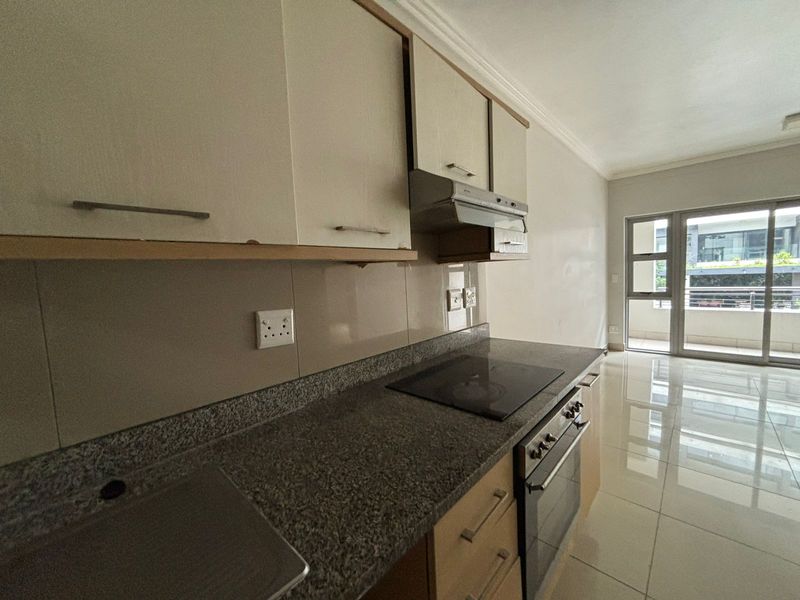 A functional kitchen featuring granite countertops, built-in oven, electric hob, and ample cabinetry, leading directly to a balcony through a sliding glass door.