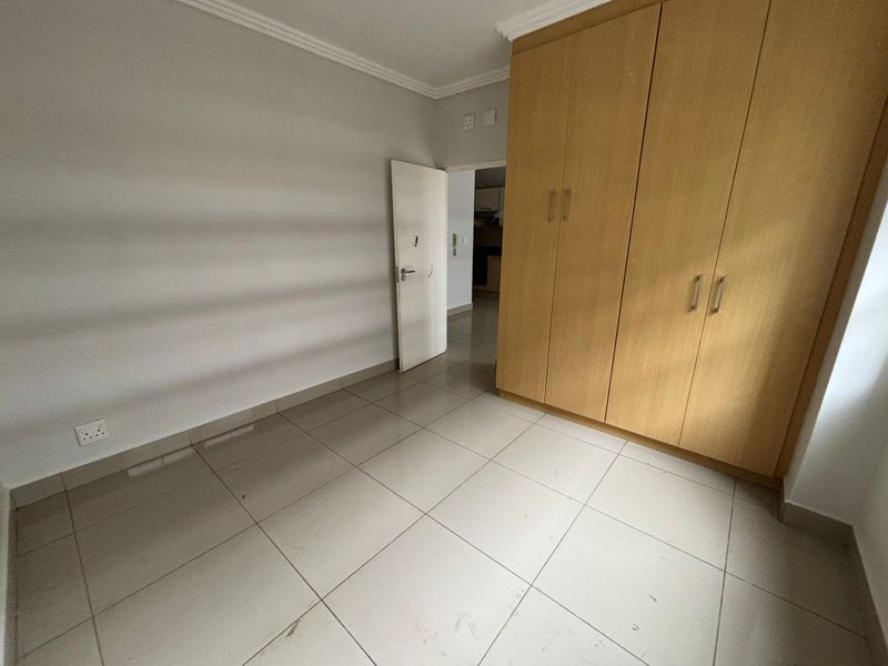 An empty bedroom featuring light-colored floor tiles, neutral walls, and a large built-in wooden wardrobe with ample storage space.