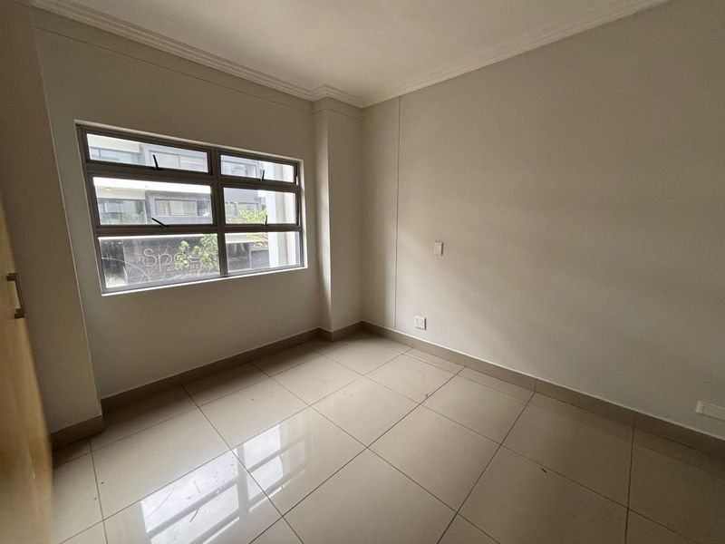 A clean, empty bedroom featuring neutral tiled flooring, large aluminium-framed windows, and minimalist finishes, ready for personalization.