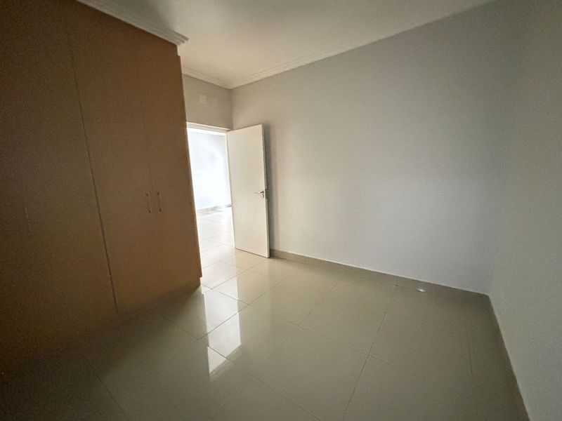 An empty bedroom featuring neutral tiled flooring and built-in wooden cupboards, offering a clean and versatile space.