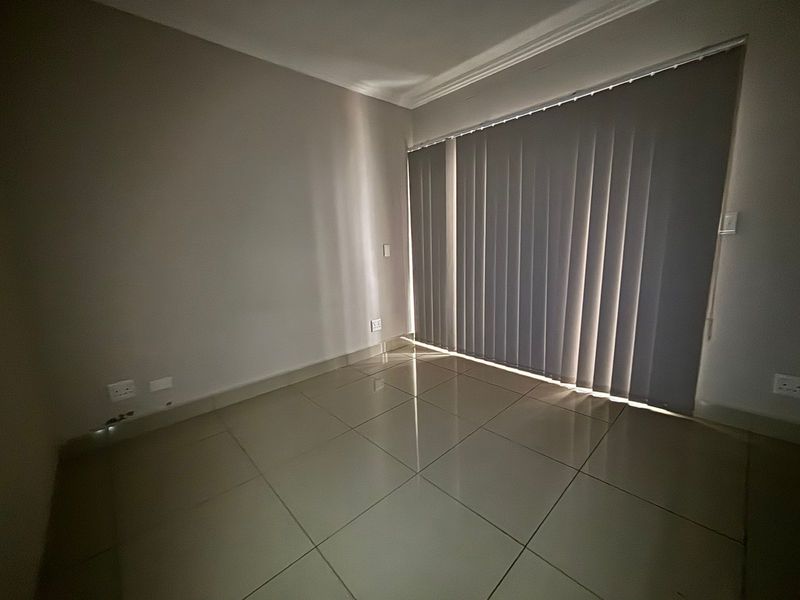 An empty bedroom featuring neutral tiled flooring, coving, and vertical blinds covering a large window or sliding door.