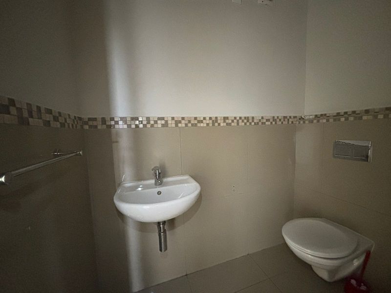 A compact bathroom featuring a wall-mounted basin, wall-hung toilet with a chrome flush plate, and neutral tiled wall accents.