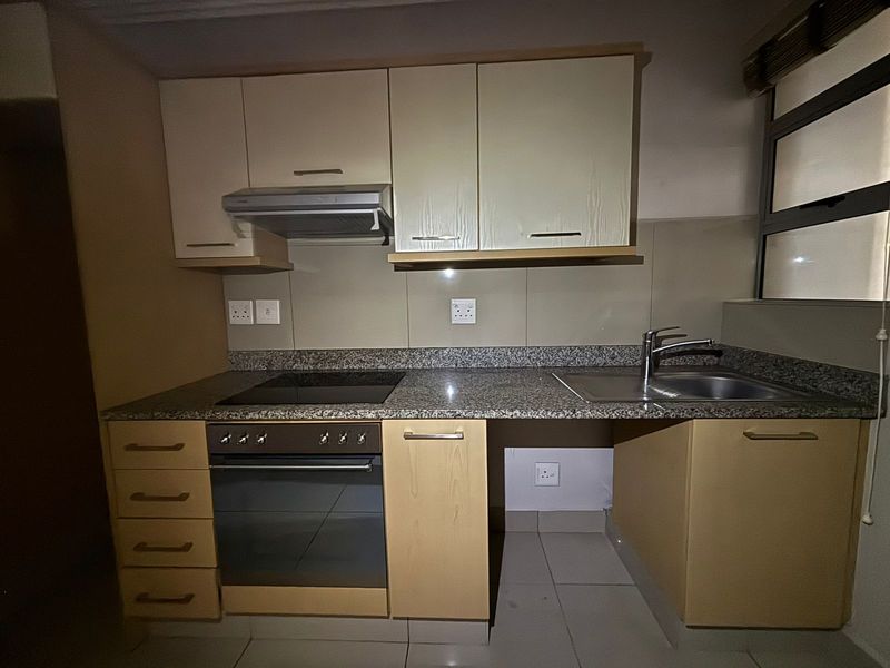 Compact kitchen featuring granite countertops, built-in oven, electric hob, extractor fan, and stainless steel sink with tiled splashback.