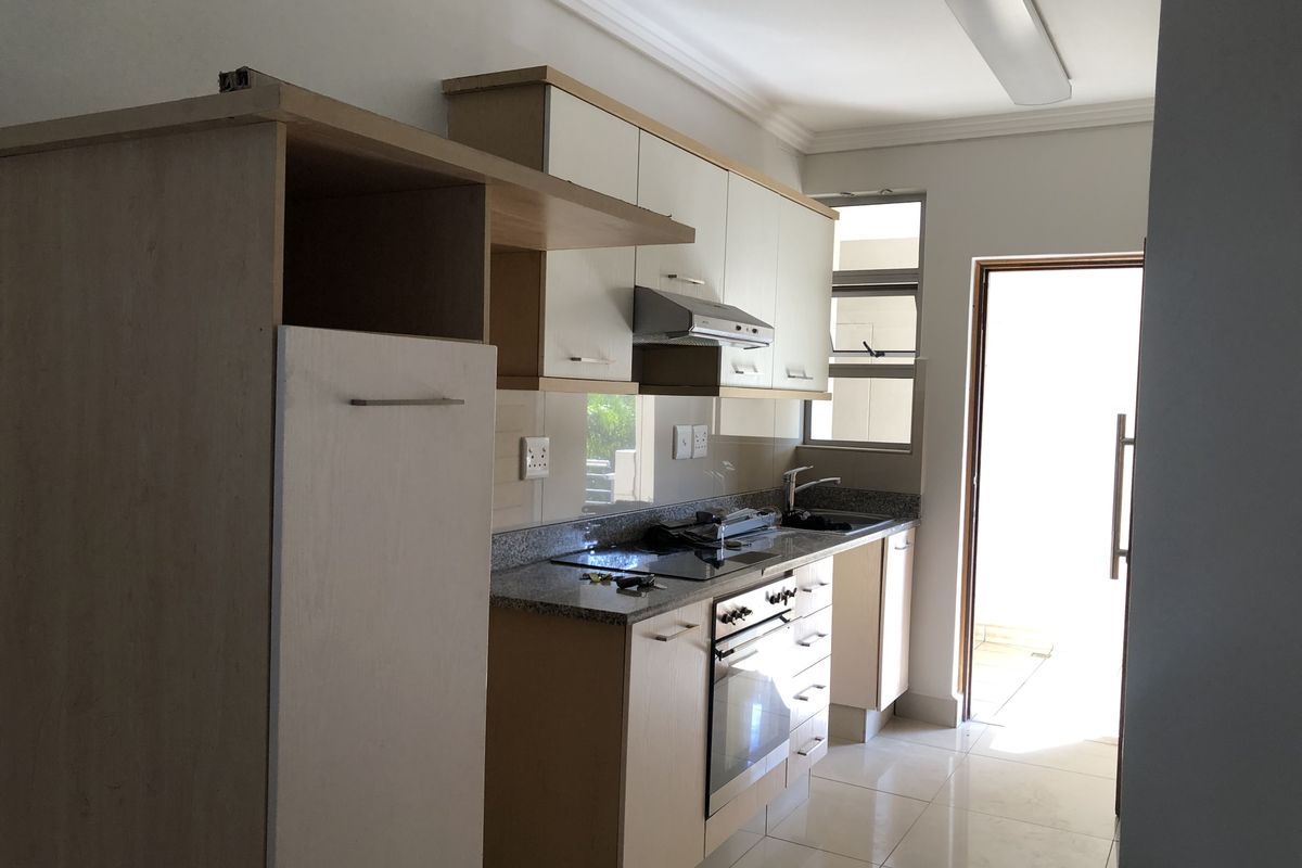 A functional kitchen featuring built-in cabinetry, granite countertops, an electric hob, oven, and extractor fan, with direct access to an outdoor area.