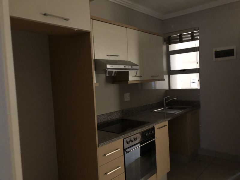 A functional kitchen featuring granite countertops, built-in oven, electric hob, extractor fan, and ample cabinetry, presented in a clean, empty state.