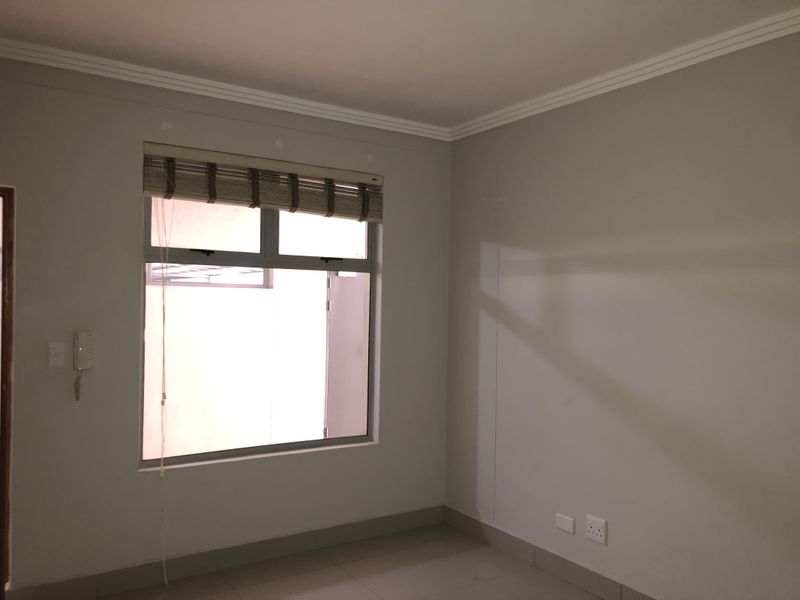 A clean, empty bedroom featuring neutral walls, tiled flooring, cornice detailing, and an integrated intercom system.