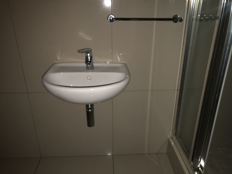 A clean, modern bathroom featuring a wall-mounted basin with chrome fixtures, tiled walls, and a glass-enclosed shower.