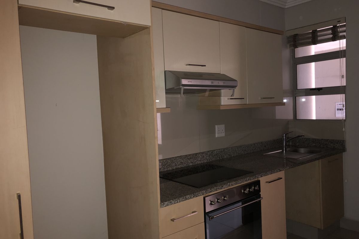 A functional kitchen featuring light wood cabinetry, granite countertops, a built-in oven, electric hob, and an integrated extractor fan.
