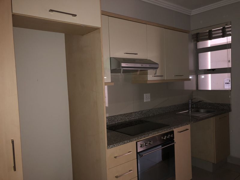 A functional kitchen featuring light wood cabinetry, granite countertops, a built-in oven, electric hob, and an integrated extractor fan.