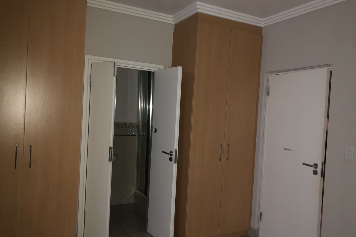 A bedroom featuring built-in wooden cupboards, tiled flooring, and direct access to an en-suite bathroom.