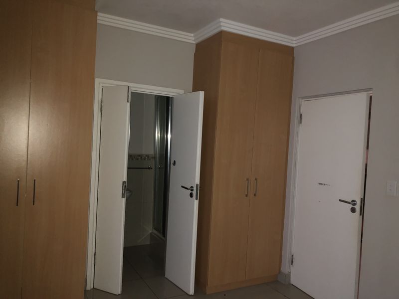 A bedroom featuring built-in wooden cupboards, tiled flooring, and direct access to an en-suite bathroom.