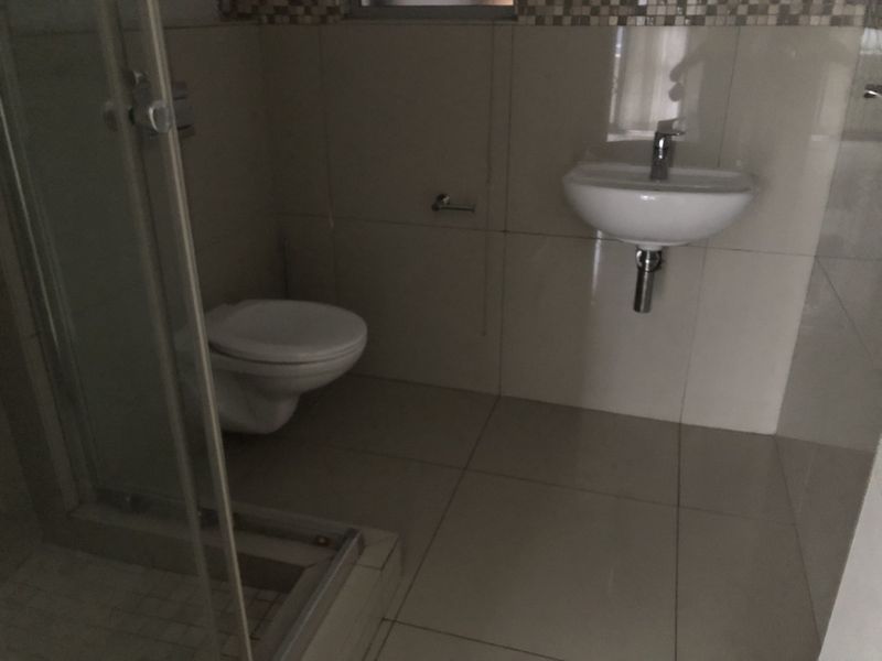 A functional bathroom featuring a wall-mounted toilet, wall-mounted basin, and a glass-enclosed shower with neutral tiled finishes.