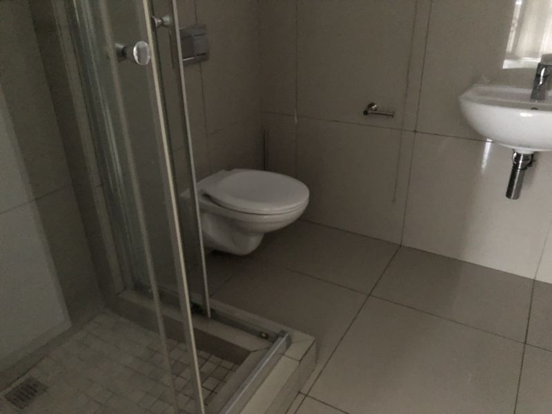 A functional bathroom featuring a wall-mounted toilet, a glass shower enclosure, and a wall-mounted basin with neutral floor and wall tiling.