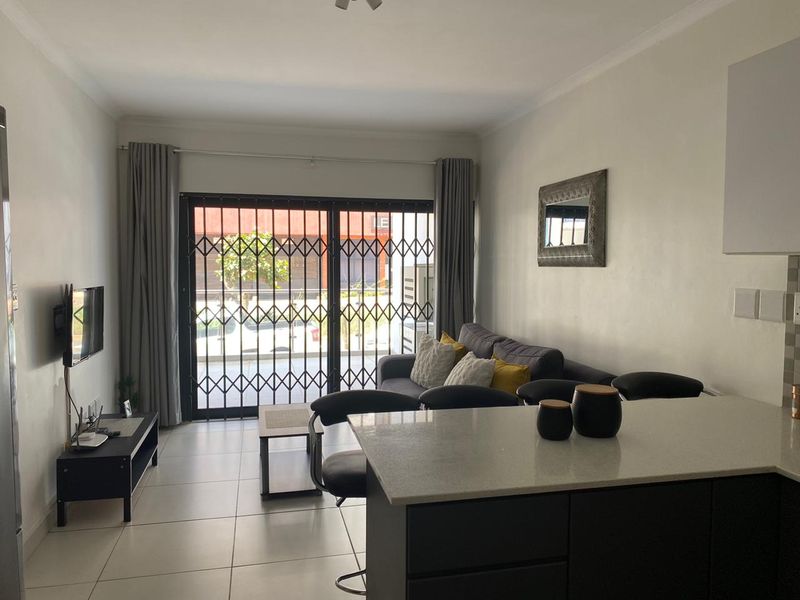 Open-plan living area featuring a modern kitchen island, tiled flooring, and a sliding glass door with security gate leading to the exterior.