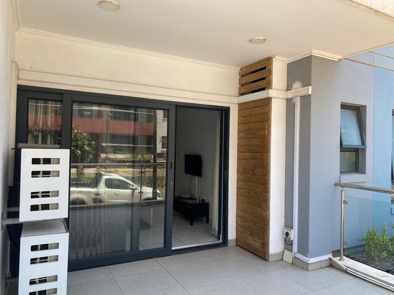 A covered balcony featuring tiled flooring, a glass balustrade, and a decorative timber slat panel, providing seamless access to the interior living space.