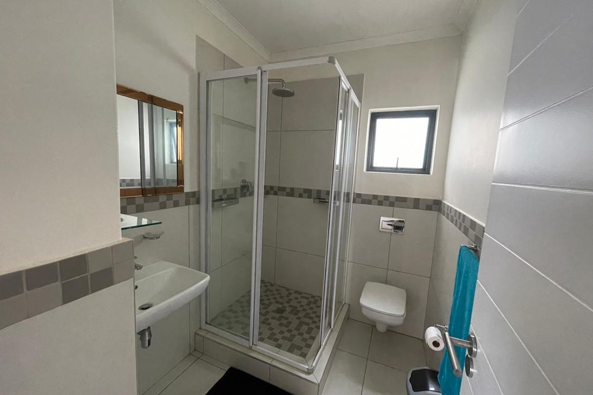 A clean and functional bathroom featuring a glass-enclosed shower, wall-mounted toilet, and a modern washbasin with a mirrored cabinet.