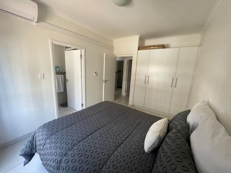 A well-maintained bedroom featuring built-in cupboards, tiled flooring, and an integrated air conditioning unit, with direct access to an en-suite bathroom.