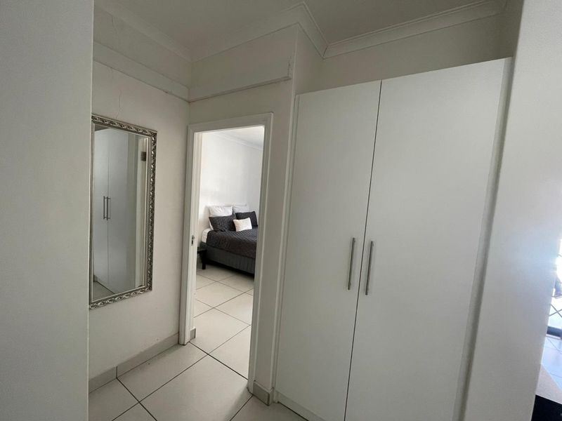 A functional hallway featuring tiled flooring and built-in cupboards, providing access to the adjacent bedroom.