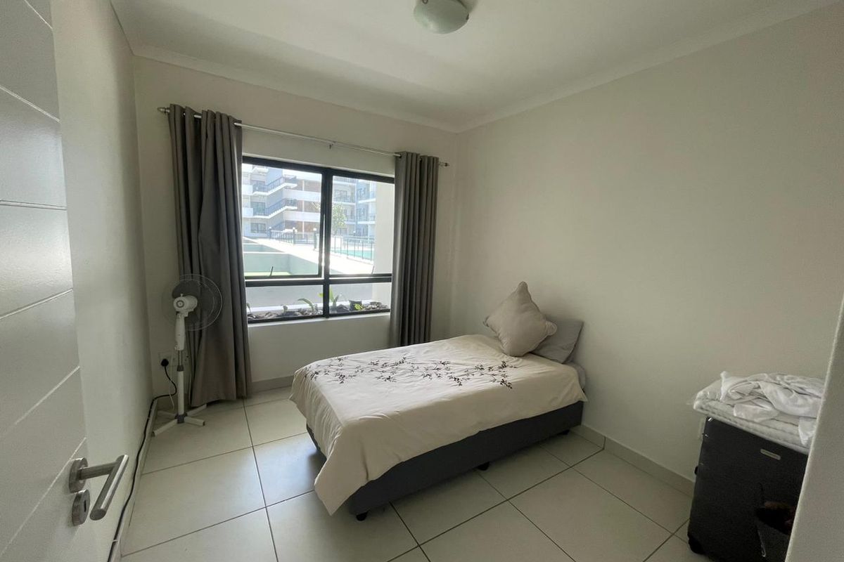 A clean, neutrally finished bedroom featuring large aluminium-framed windows, tiled flooring, and a simple ceiling light fixture.