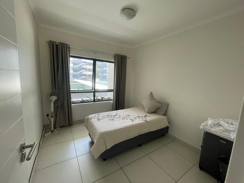 A clean, neutrally finished bedroom featuring large aluminium-framed windows, tiled flooring, and a simple ceiling light fixture.