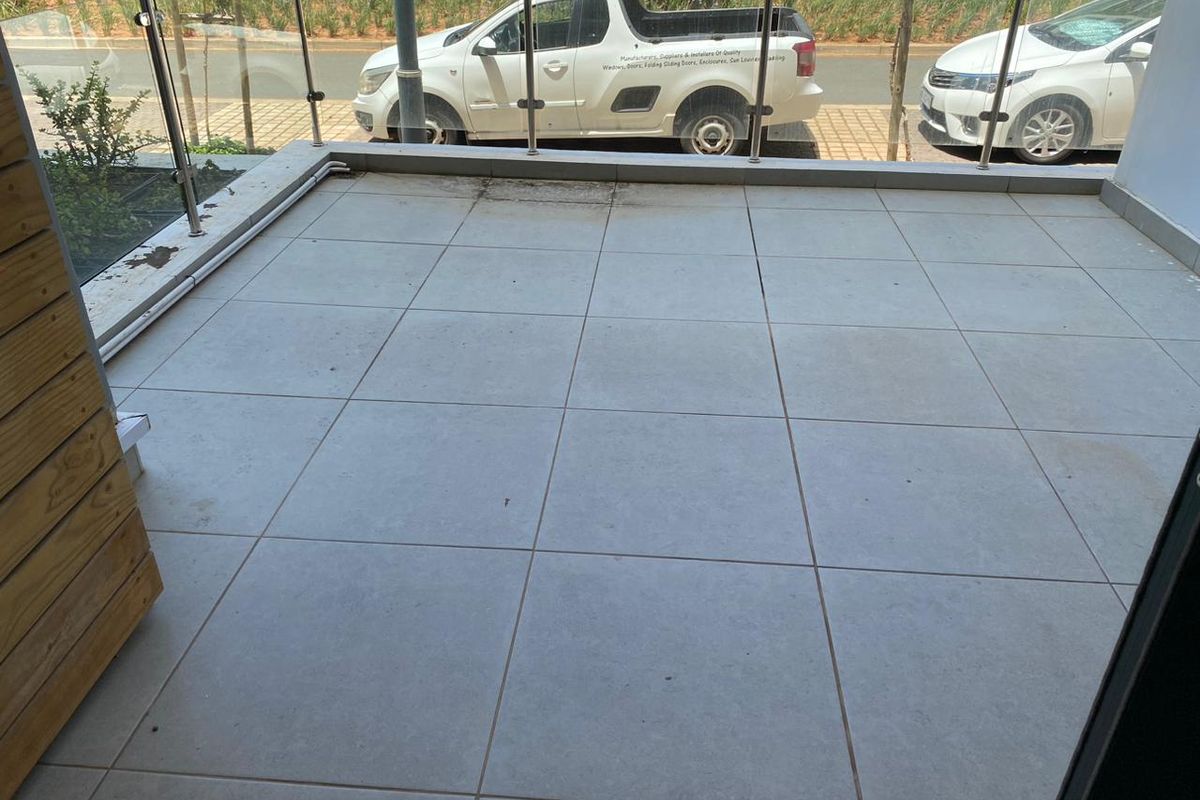 A tiled balcony featuring a modern glass balustrade, offering an open outdoor space suitable for seating or container gardening.