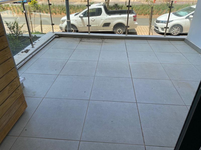 A tiled balcony featuring a modern glass balustrade, offering an open outdoor space suitable for seating or container gardening.