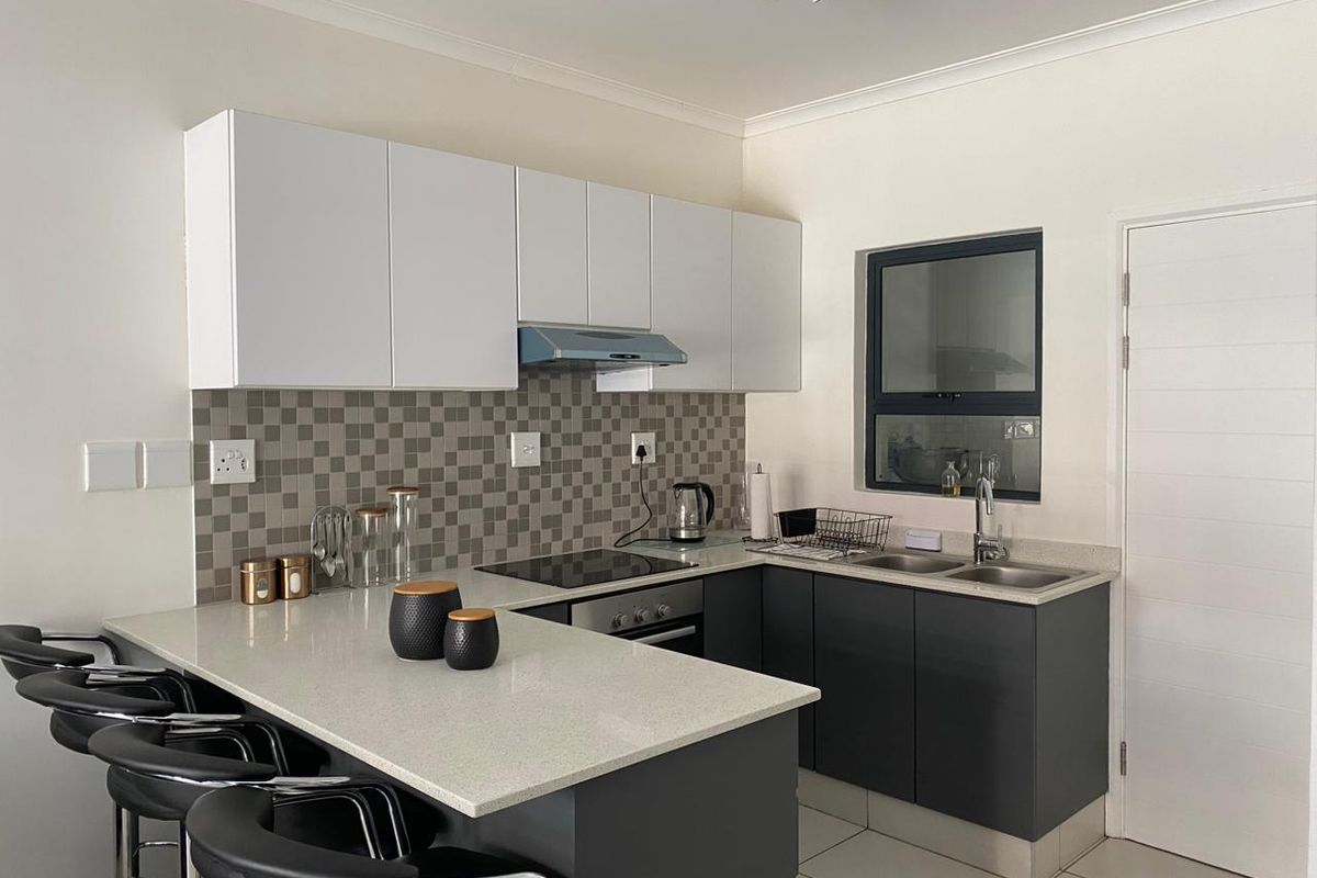 Modern kitchen featuring dark grey lower cabinetry, white upper cabinets, stone countertops, a breakfast bar, and a mosaic tile backsplash.