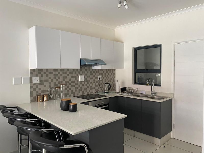 Modern kitchen featuring dark grey lower cabinetry, white upper cabinets, stone countertops, a breakfast bar, and a mosaic tile backsplash.