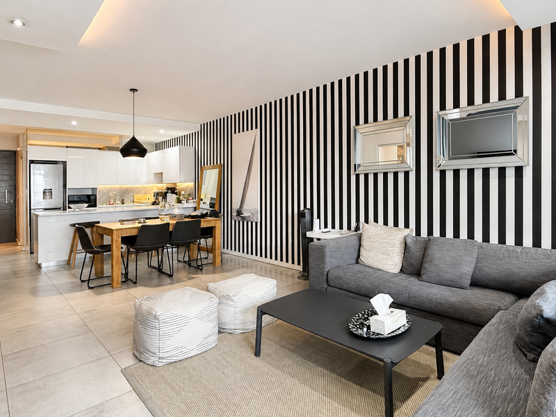 Spacious open-plan living and dining area featuring a modern kitchen with sleek cabinetry, stone countertops, and integrated appliances, complemented by contemporary tiled flooring.