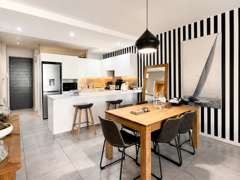 Modern open-plan kitchen and dining area featuring sleek white cabinetry, stone countertops, a breakfast bar, and contemporary tiled flooring.