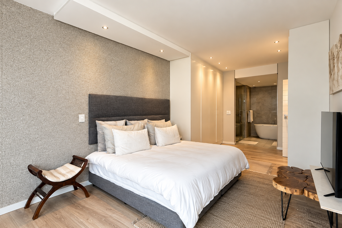 Modern bedroom featuring a textured feature wall, integrated wardrobe storage, recessed lighting, and direct access to a contemporary en-suite bathroom.