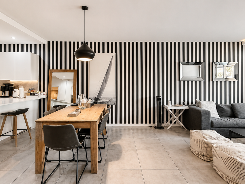 Modern open-plan living and dining area featuring sleek white kitchen cabinetry, stone countertops, tiled flooring, and a striking striped feature wall.