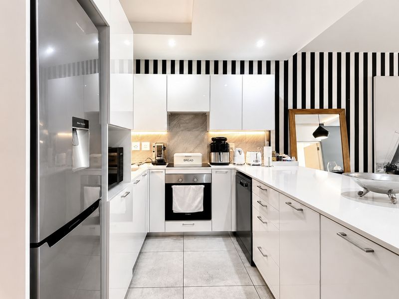 Modern kitchen featuring high-gloss white cabinetry, stone countertops, integrated appliances, and a sleek, contemporary design with recessed lighting.