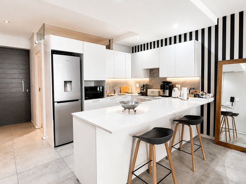 Modern kitchen featuring sleek white cabinetry, stone countertops, a functional island, and integrated appliances, complemented by contemporary tiled flooring and stylish accent wall.