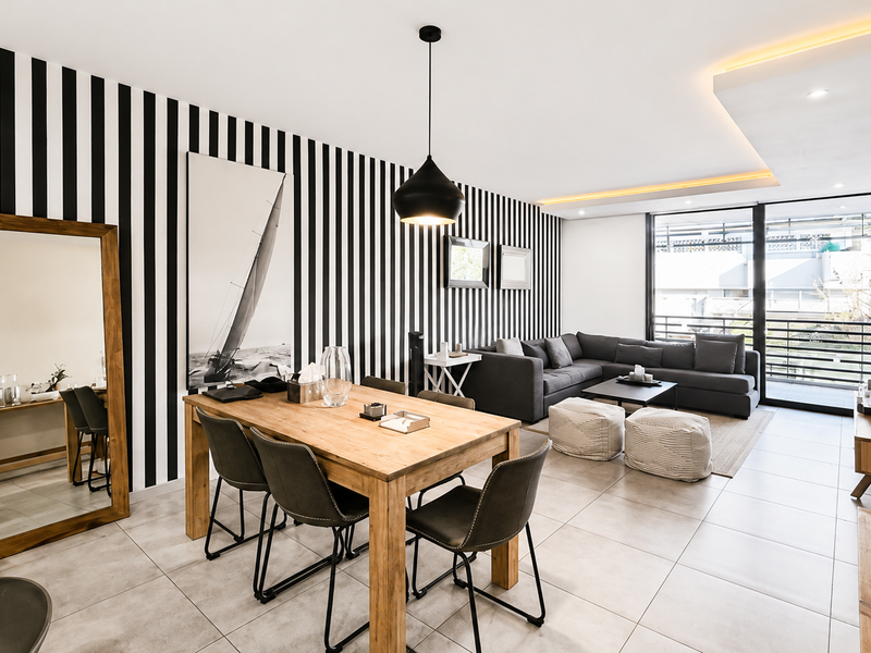 A modern open-plan living and dining area featuring tiled floors, recessed ceiling lighting, and large sliding glass doors leading to a balcony.