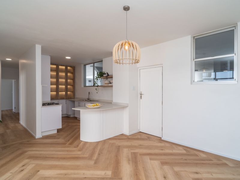 Modern open-plan living area featuring herringbone wood flooring, a sleek kitchen with fluted island, stone countertops, and integrated cabinetry with warm accent lighting.