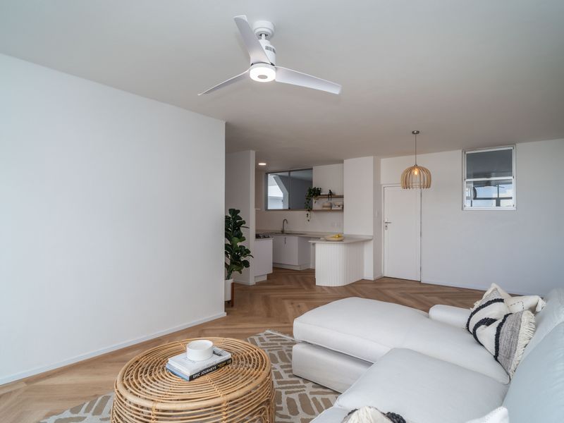 Bright open-plan living area featuring herringbone wood flooring, a modern ceiling fan, and a functional kitchen with clean cabinetry and countertops.