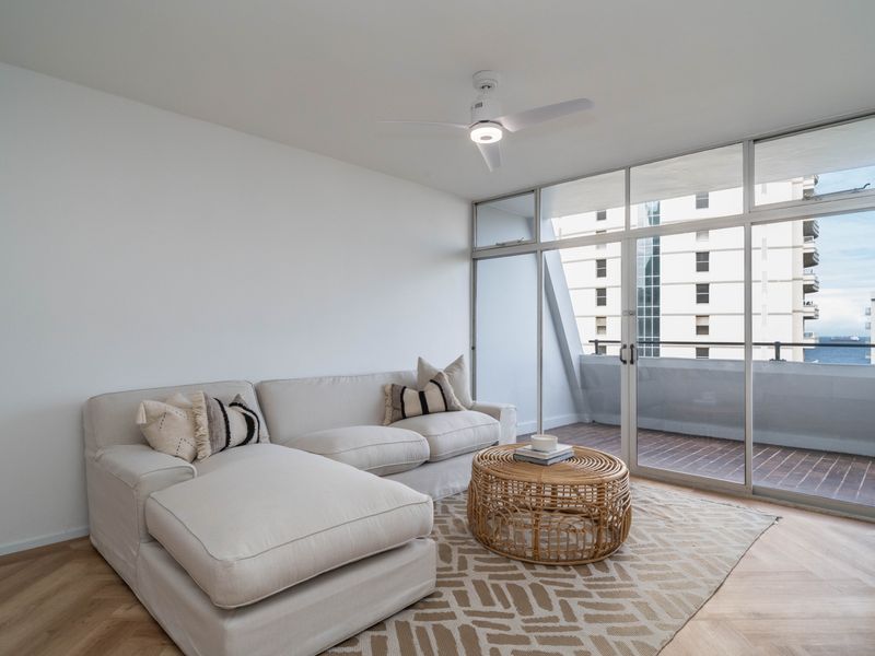 Bright living room featuring herringbone wood flooring, a modern ceiling fan, and large floor-to-ceiling windows providing access to a private balcony.