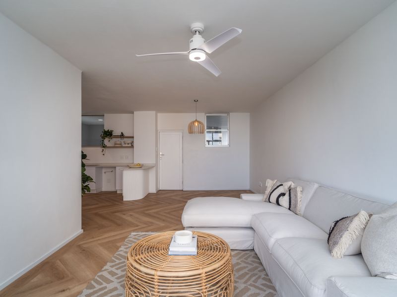 Bright open-plan living area featuring herringbone timber flooring, a modern ceiling fan, and a functional kitchen peninsula with built-in cabinetry.