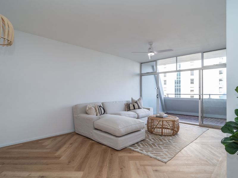 Bright and modern living room featuring herringbone timber flooring, a ceiling fan, and large sliding glass doors leading to an outdoor balcony.