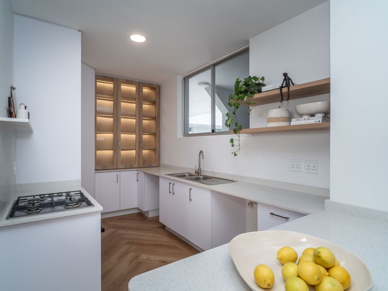 Modern kitchen featuring white cabinetry, stone countertops, a gas hob, and elegant herringbone flooring with integrated display lighting.