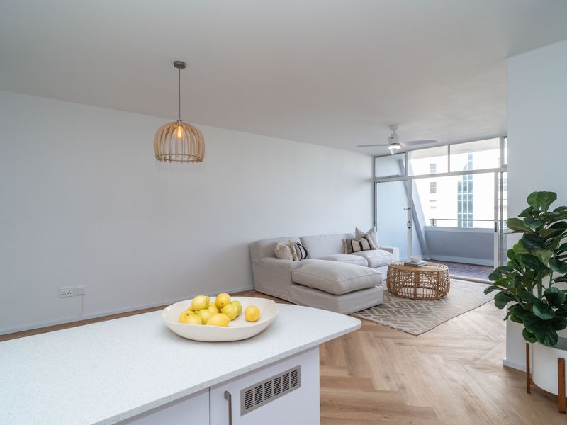 Bright open-plan living area featuring modern herringbone timber flooring, a sleek kitchen island, and seamless access to a private balcony.