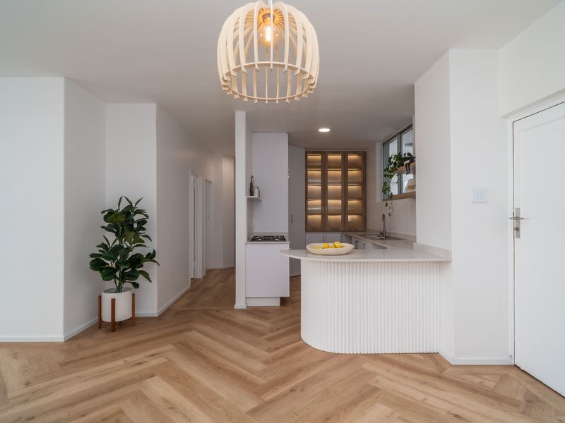 Modern open-plan kitchen featuring herringbone wood flooring, a fluted island, stone countertops, and integrated cabinetry with warm accent lighting.