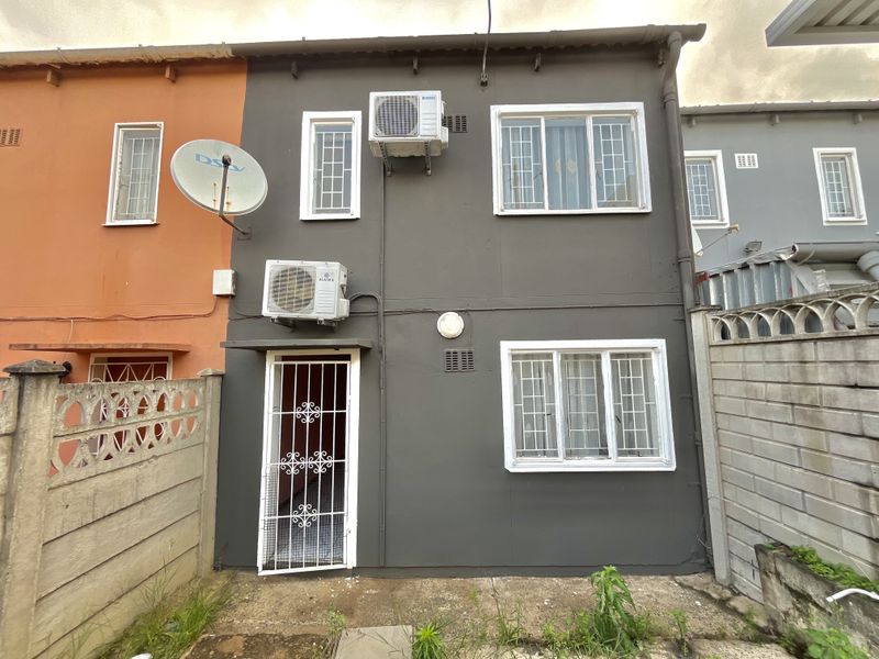 Rear elevation of a townhouse featuring dark grey exterior paint, security gates, burglar bars, and two wall-mounted air conditioning units.