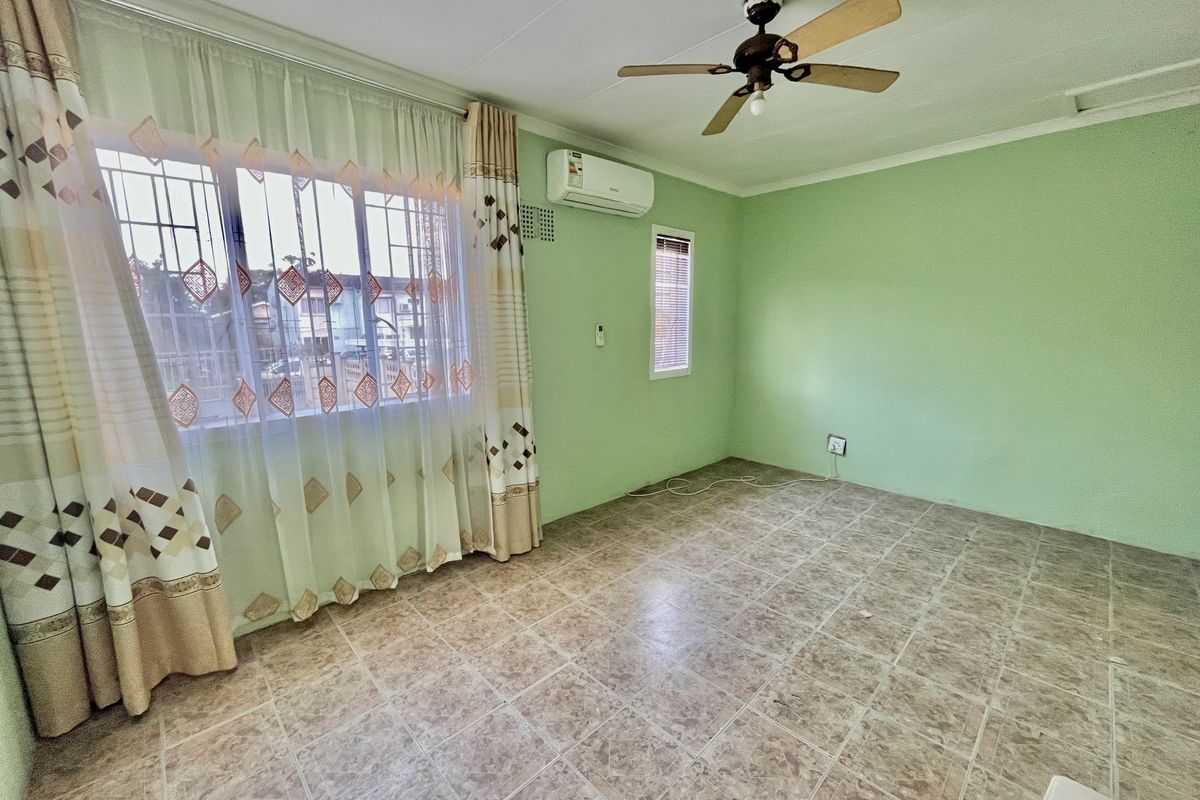 A spacious, empty bedroom featuring tiled flooring, a ceiling fan, and a wall-mounted split-system air conditioner, providing a comfortable and functional living space.