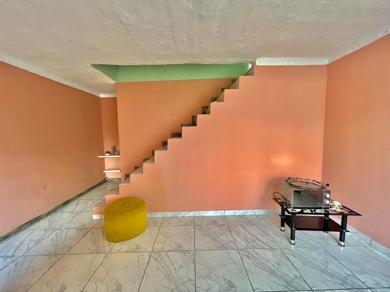 An open-plan living area featuring a central staircase, marble-look tiled flooring, and built-in wall shelving, awaiting modern updates to the wall finishes.