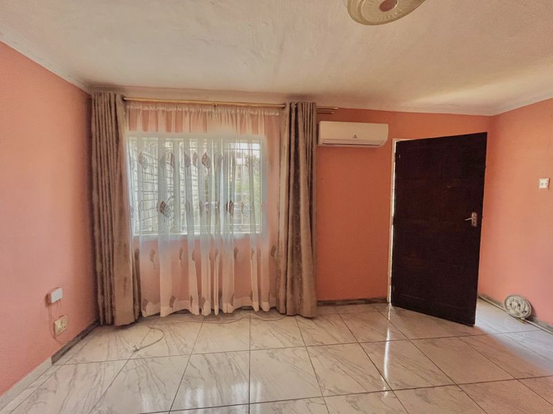 An empty living room featuring tiled flooring, an installed air conditioning unit, and a window with curtains.