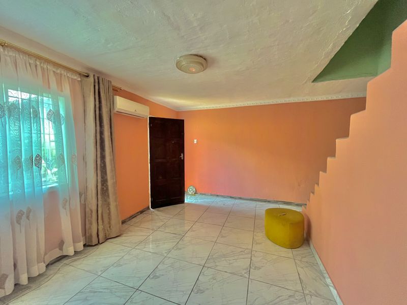 An empty living room featuring tiled flooring, a split-system air conditioner, and a staircase, awaiting personalization and updated finishes.