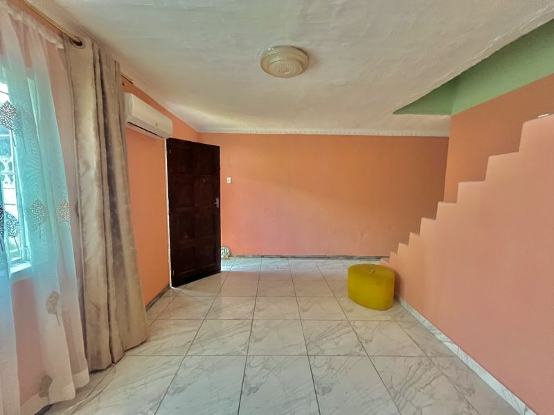 An open-plan living area featuring tiled flooring, a built-in staircase, and a wall-mounted air conditioning unit, ready for modern interior updates.